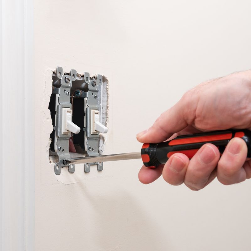 Electrician using a screwdriver to remove a wall switch and check the wiring behind it